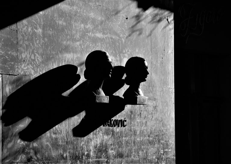 Black and white photo of the shadows of sculpted busts on a weathered wall