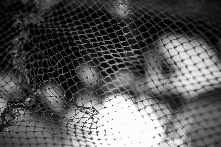 Black and white close-up of a fishing net with soft out-of-focus light