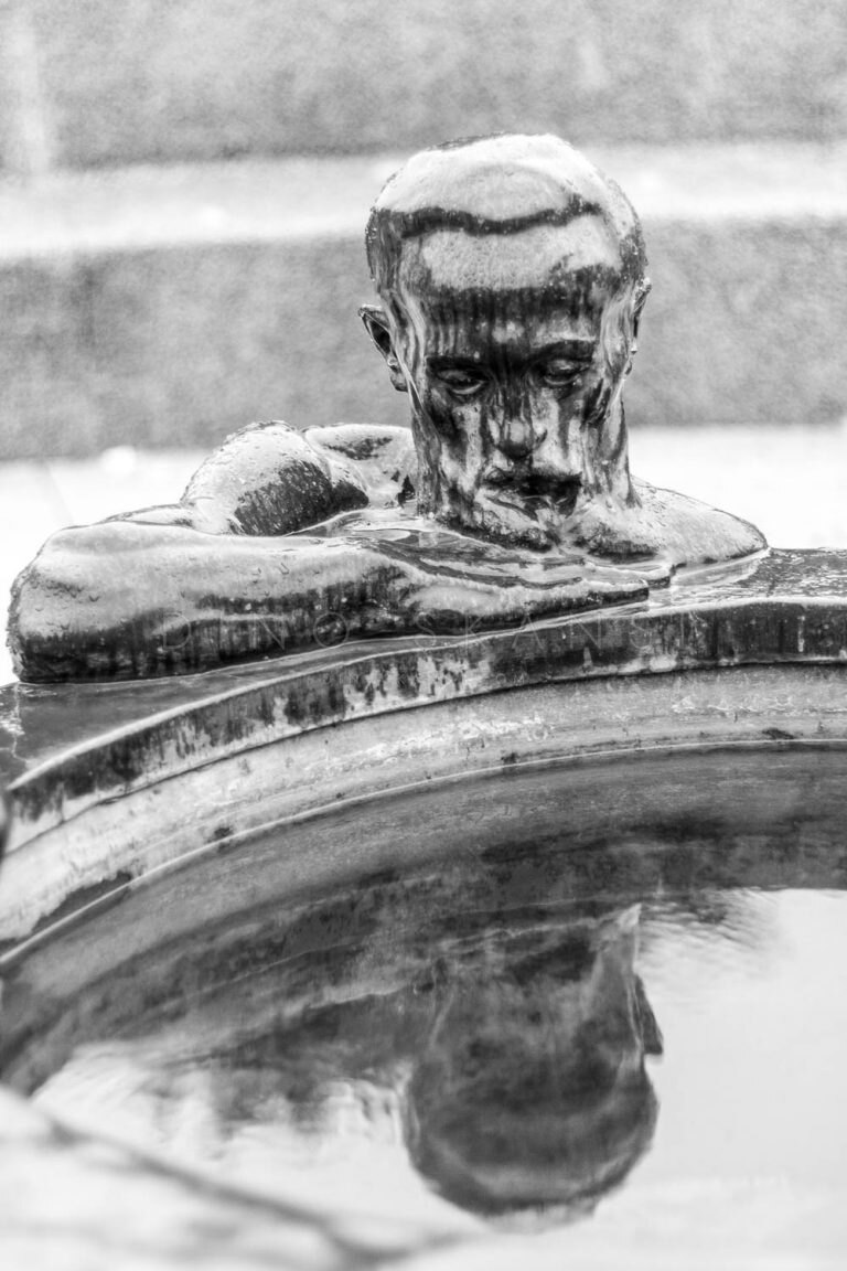 Black and white photo of a bronze fountain sculpture of a man's head and arms
