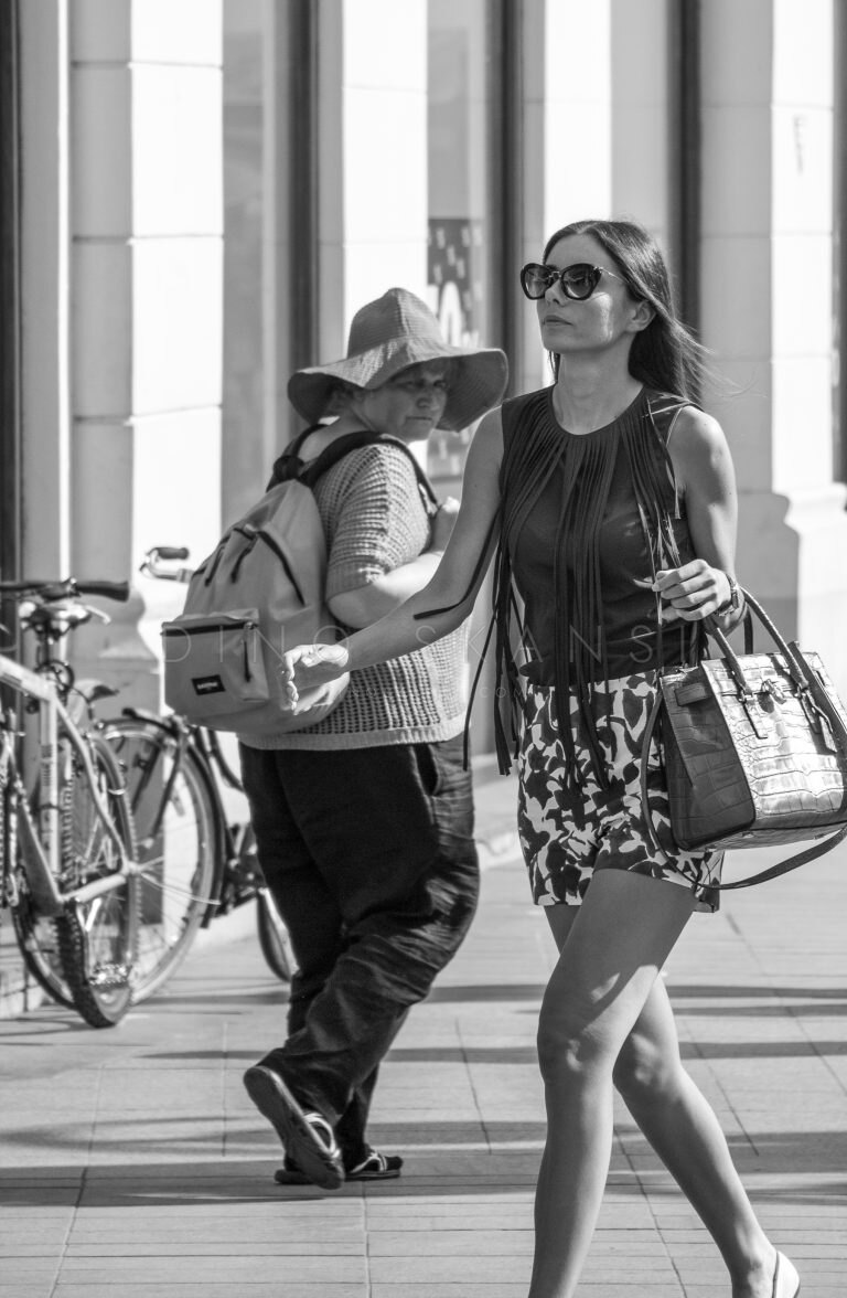 Colour street photo of a woman in sunglasses and a man in a hat crossing paths