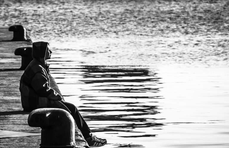 Black and white photo of a person sitting by rippling water