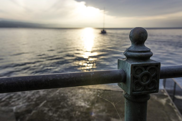 Sunset over a calm sea seen past a stone railing post