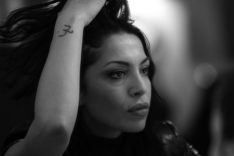 Black and white profile portrait of a woman with dark hair, arm raised to her head
