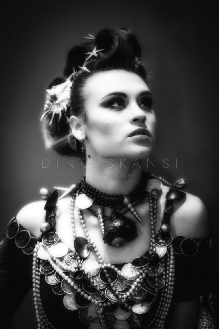 Black and white portrait of a woman with a hair ornament and layered necklaces, looking up