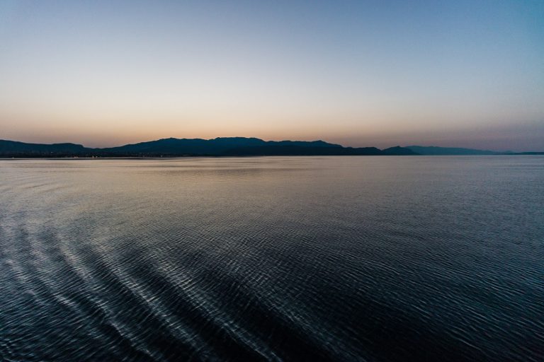 Calm sea at dusk with a distant shoreline under a pastel sky