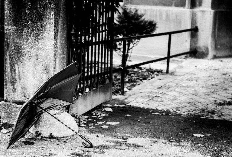 Black and white photo of an umbrella lying by iron railings on a snowy street