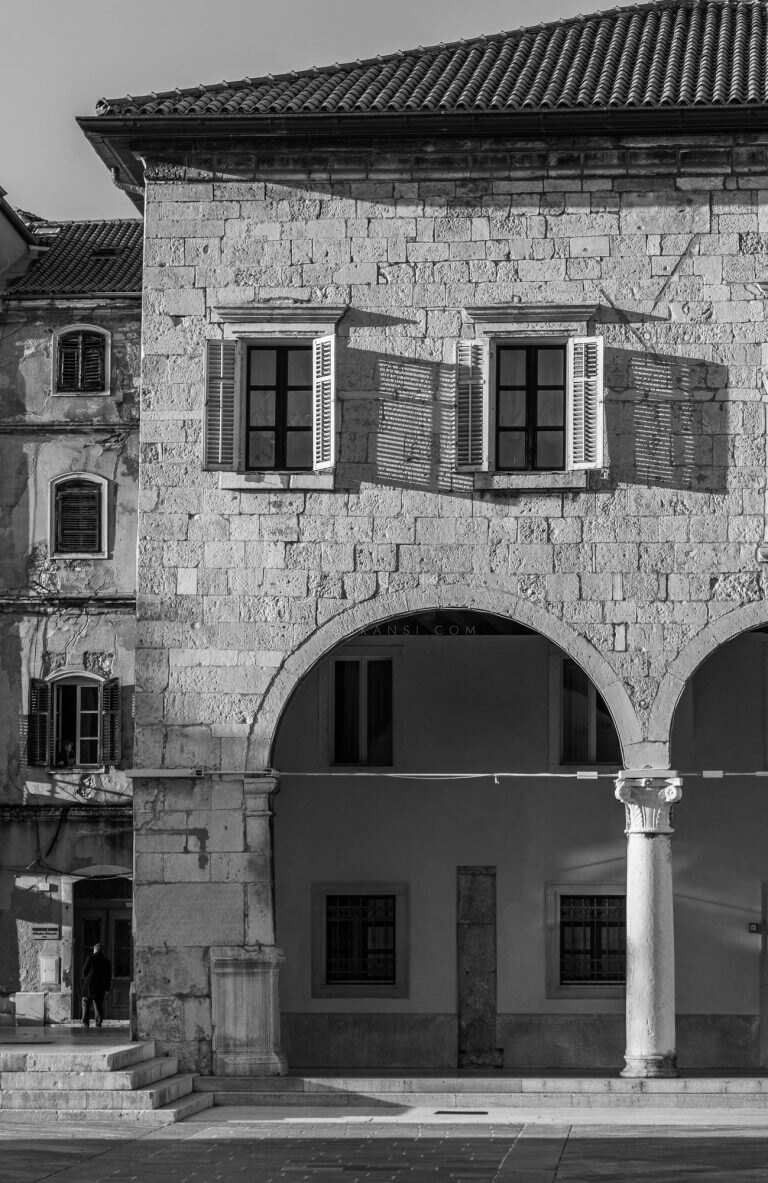 Black and white photo of a stone house with shutters and an arched loggia