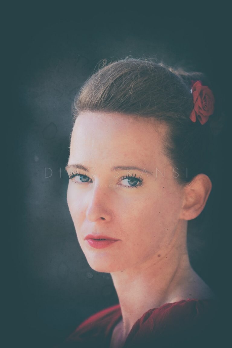 Colour portrait of a woman with pinned-up hair and a flower against a teal background