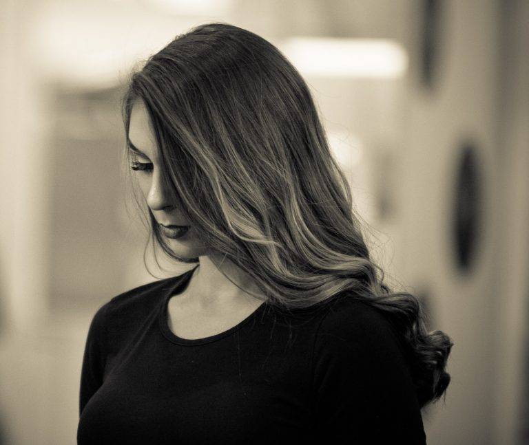 Colour portrait of a woman with long wavy hair looking down, in a black top
