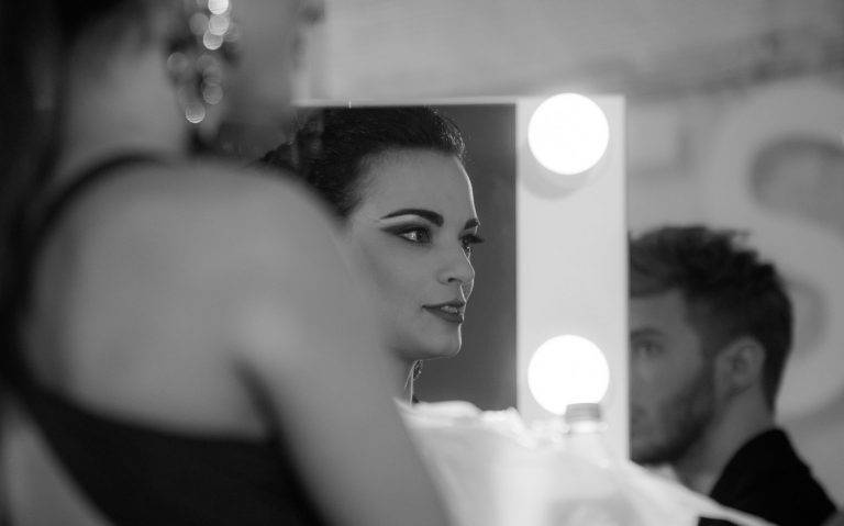 Black and white portrait of a woman reflected in a backstage make-up mirror