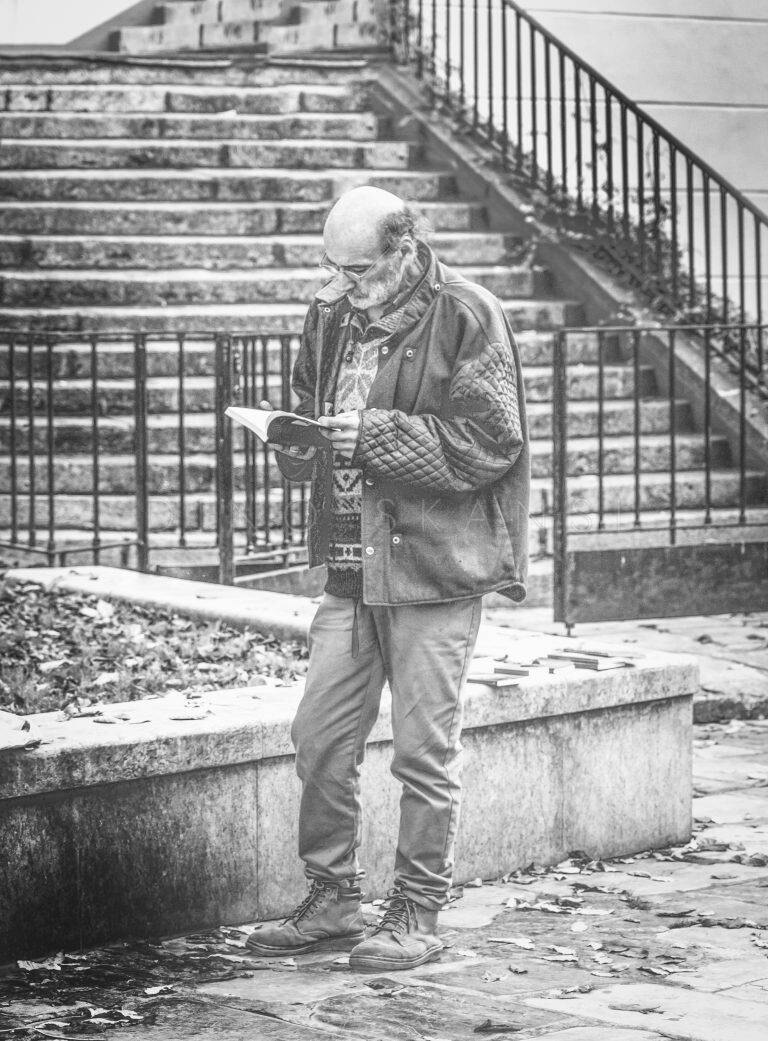 Black and white photo of an elderly man reading while standing in front of stone steps