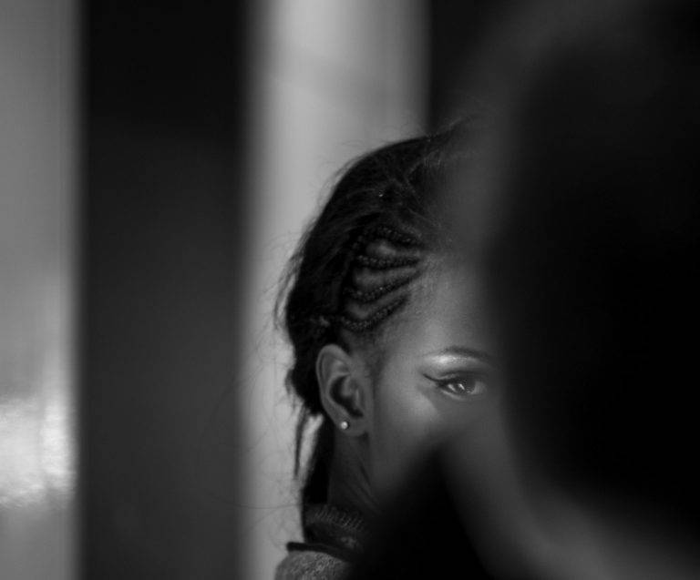 Black and white portrait of a woman with braided hair seen from behind, partly in shadow