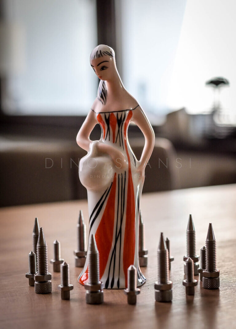 Ceramic figurine of a woman with a jug standing among small metal pieces