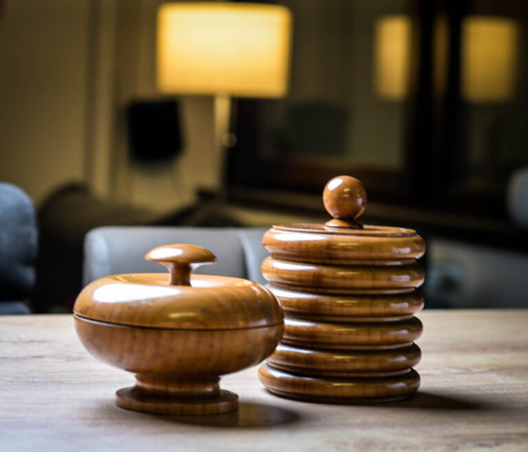 Two carved wooden lidded boxes on a table in warm lamp light