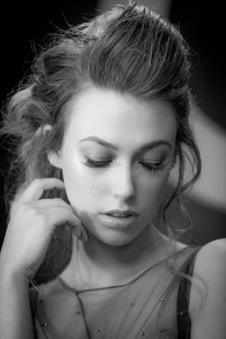 Black and white portrait of a woman with her hair up, hand at her neck, eyes lowered