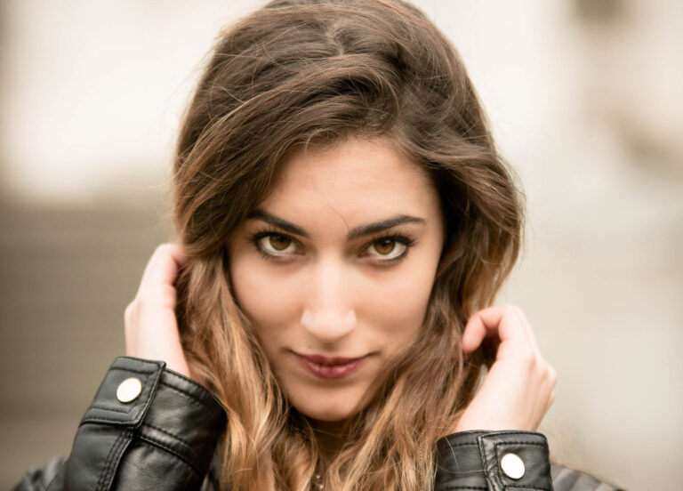Colour portrait of a woman with long wavy hair, hands raised to her head