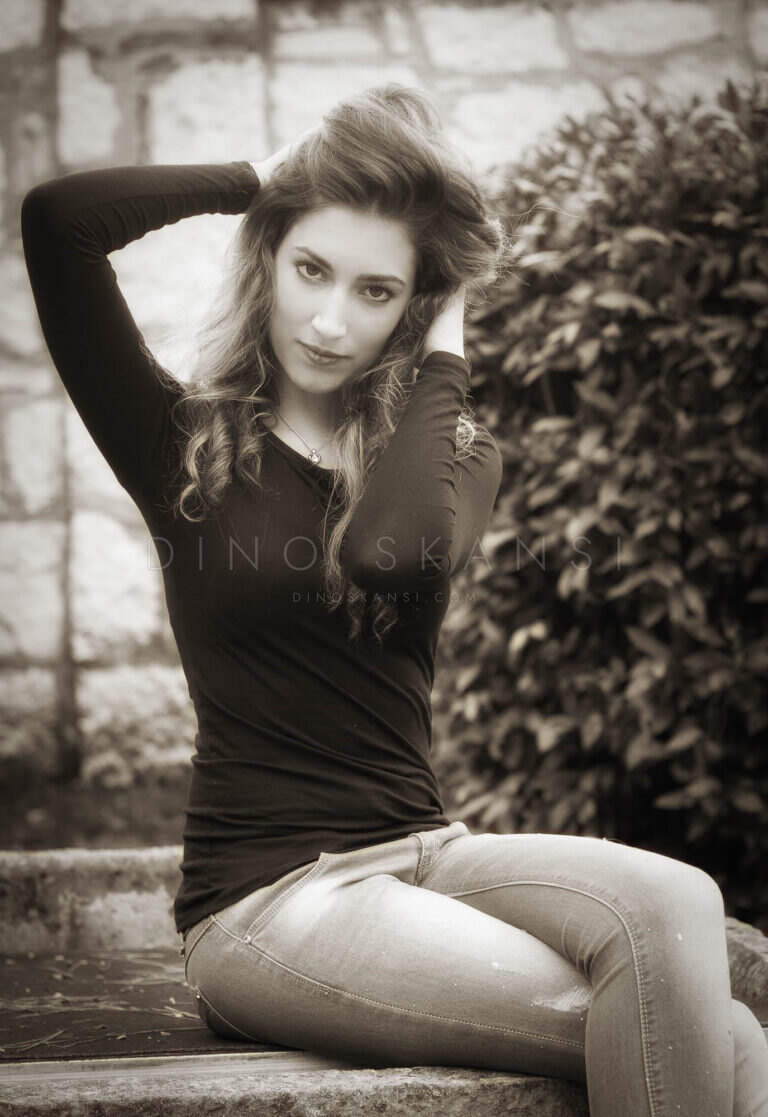 Black and white portrait of a woman sitting by a hedge with her arm raised