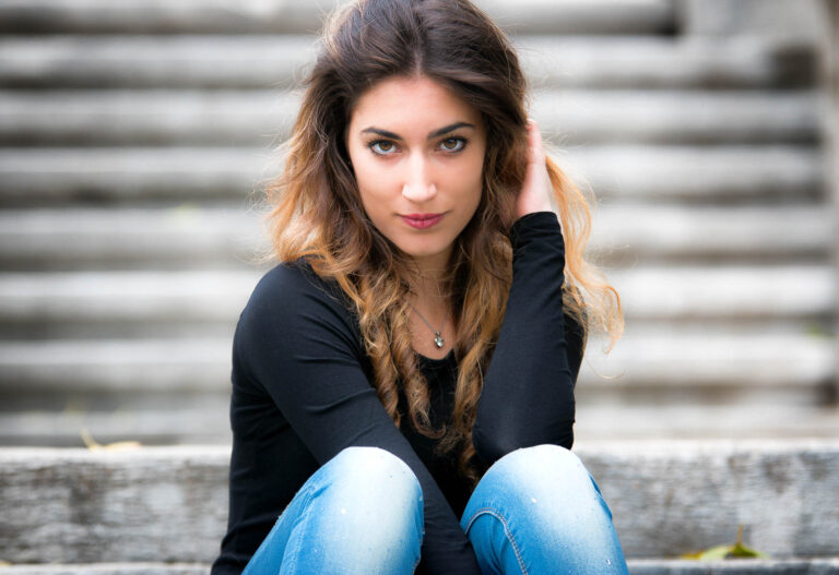 Colour portrait of a woman in a black top and jeans sitting on stone steps