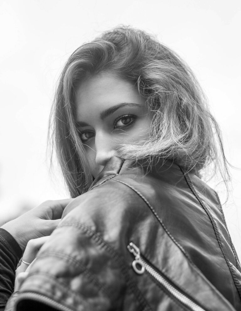 Black and white portrait of a woman peeking over the shoulder of her leather jacket