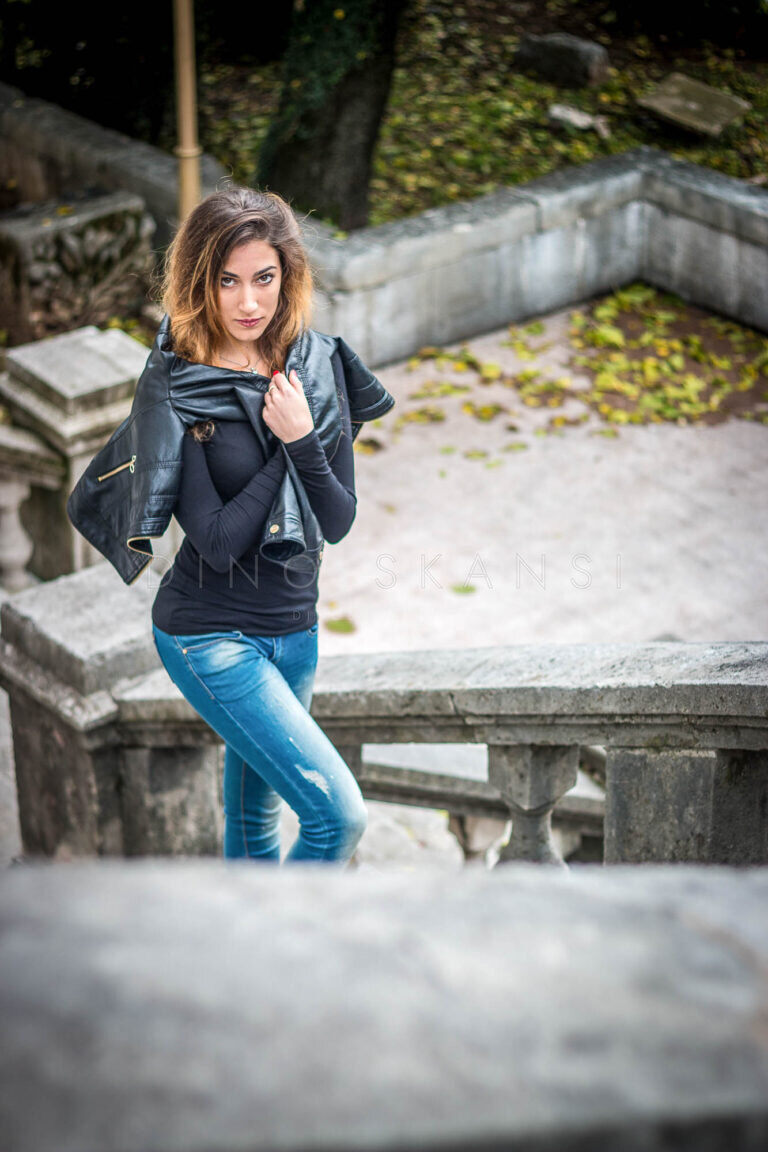 Colour portrait of a woman in a leather jacket and jeans leaning on a stone balustrade