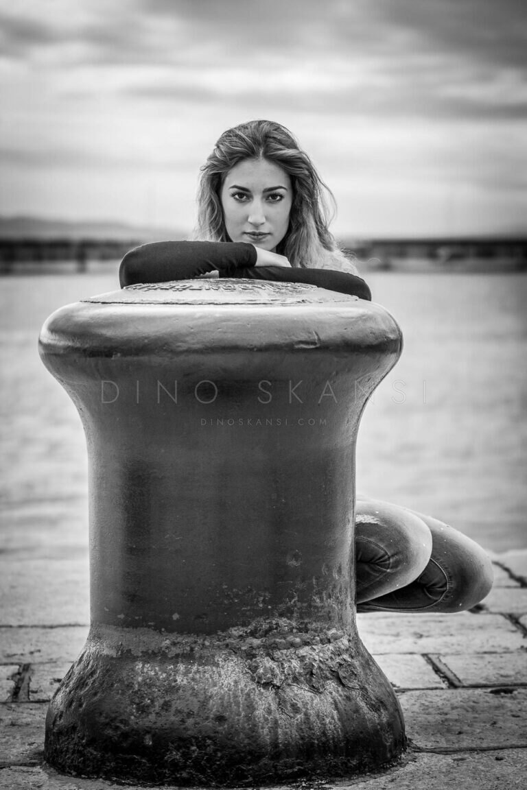 Black and white photo of a woman peeking over a harbour mooring bollard