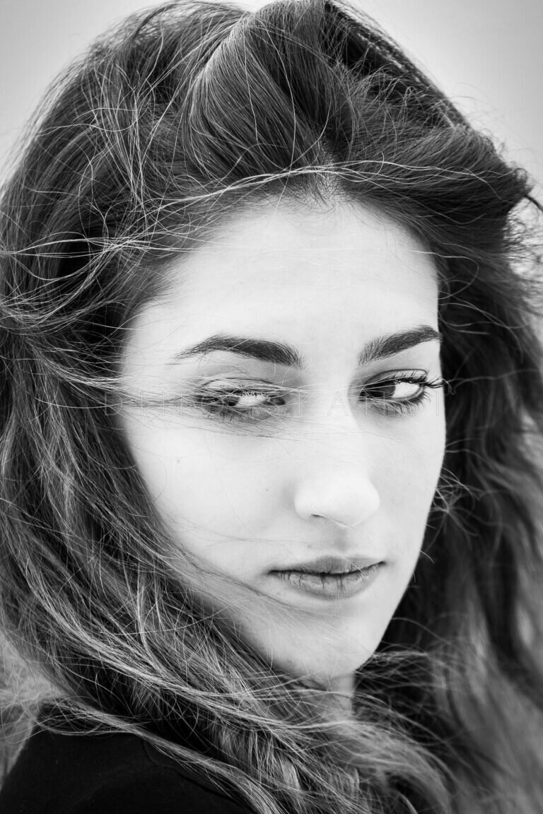 Black and white close-up of a woman with wind-blown hair looking down