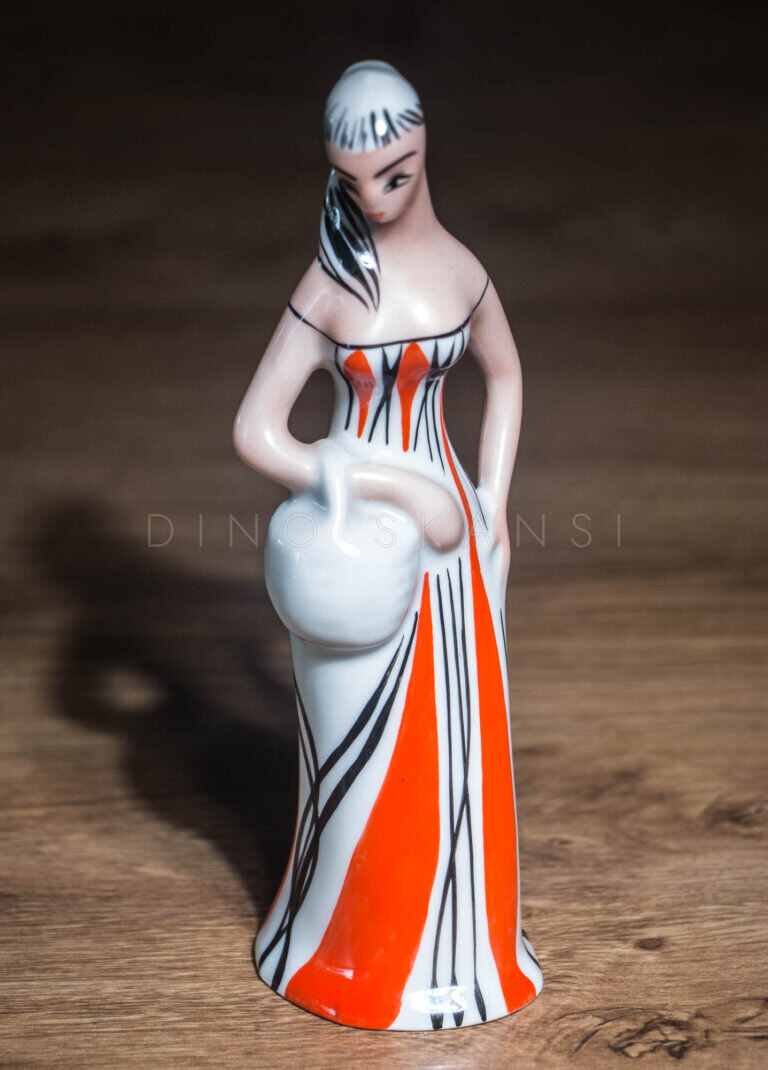 Close-up of a ceramic figurine of a woman in a red striped dress holding a jug