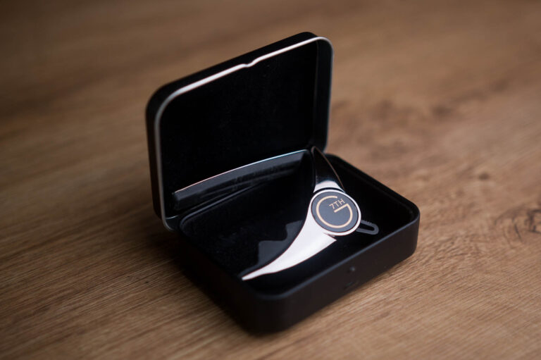 Open black case holding a small silver accessory on a wooden table