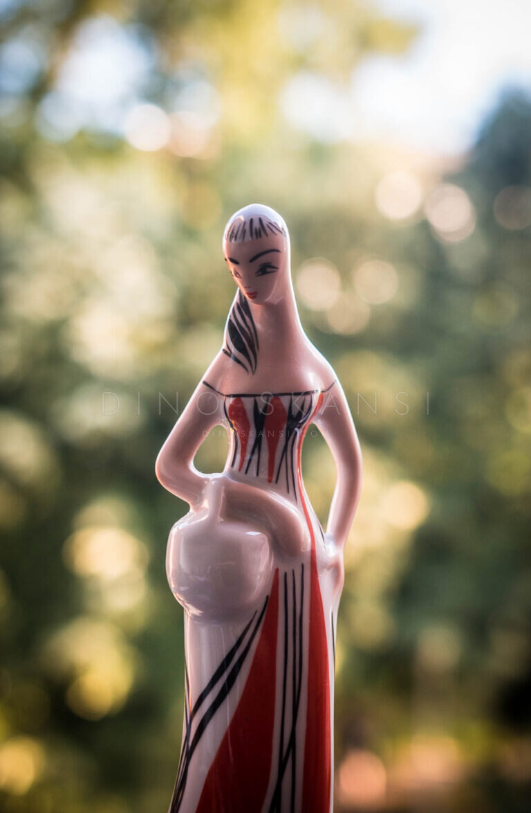 Ceramic figurine of a woman with a jug against a blurred green garden background