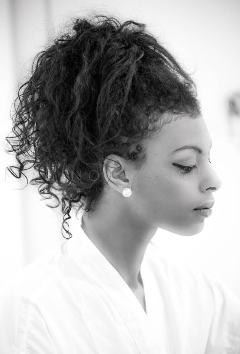 Black and white profile portrait of a woman with curly hair tied up, wearing an earring