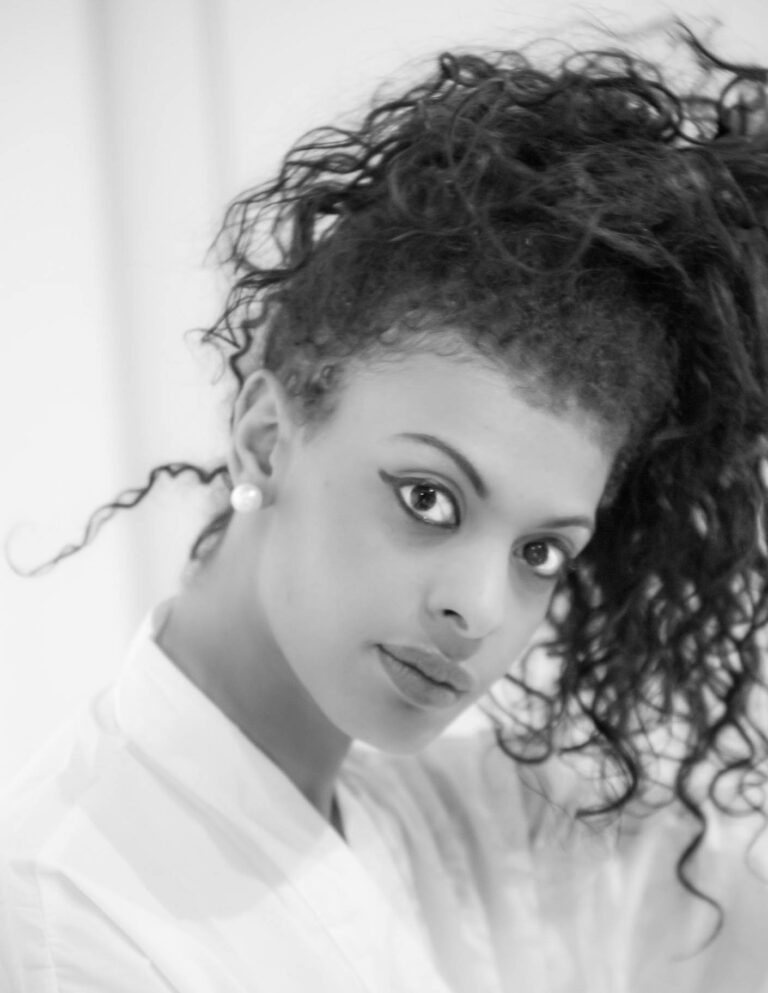 Black and white portrait of a woman with curly hair looking down over her shoulder