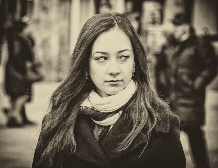 Black and white portrait of a young woman with long hair and a scarf on a city street